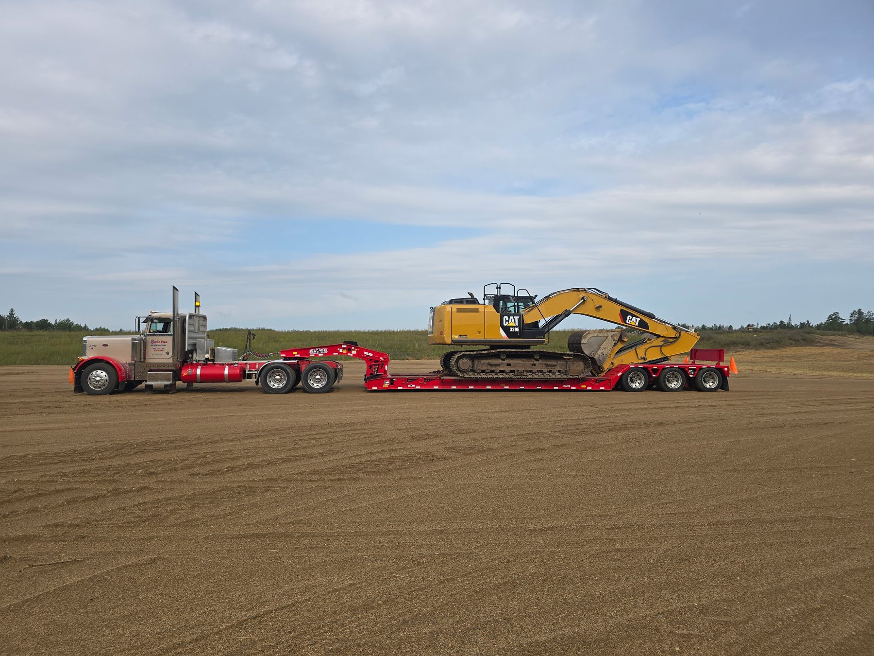 Red Storlie semi hauling an excavator on a lowboy trailer