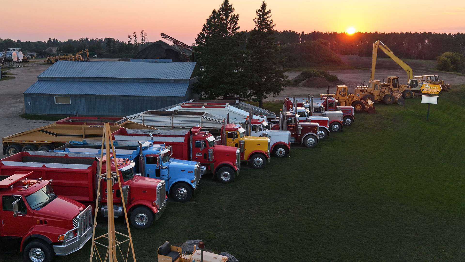 Storlie dump trucks and heavy equipment lined up at the Highway 2 yard at sunset